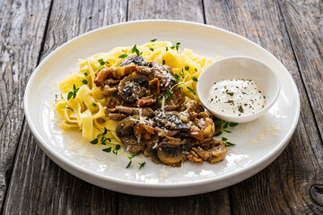 Tagliatelle with fried chicken breast nuggets, parmesan cheese and white mushrooms served on wooden table
