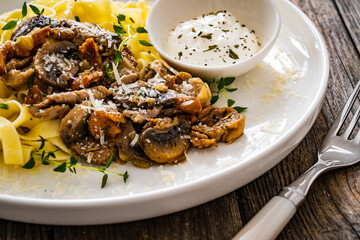 Tagliatelle with fried chicken breast nuggets, parmesan cheese and white mushrooms served on wooden table

