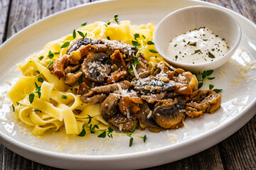 Tagliatelle with fried chicken breast nuggets, parmesan cheese and white mushrooms served on wooden table
