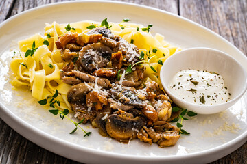 Tagliatelle with fried chicken breast nuggets, parmesan cheese and white mushrooms served on wooden table
