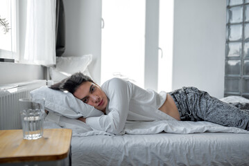 Fototapeta premium Young handsome serious man looks at camera lying on the bed in bedroom at home in the morning, close up side view photo.sick guy cannot get up, illness