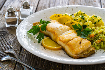 Fish dish - fried halibut with boiled potatoes and cabbage salad on wooden table