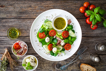 Fresh salad - prosciutto di Parma, mozzarella, cucumber, tomatoes and leafy vegetables on wooden...