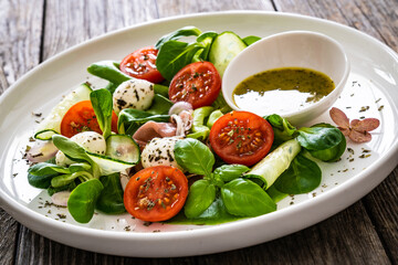 Fresh salad - prosciutto di Parma, mozzarella, cucumber, tomatoes and leafy vegetables on wooden table
