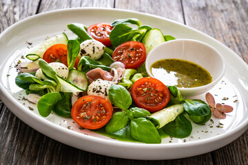 Fresh salad - prosciutto di Parma, mozzarella, cucumber, tomatoes and leafy vegetables on wooden table
