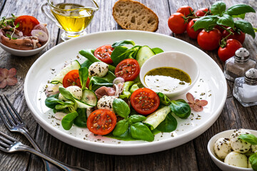 Fresh salad - prosciutto di Parma, mozzarella, cucumber, tomatoes and leafy vegetables on wooden table
