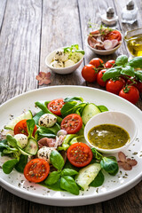 Fresh salad - prosciutto di Parma, mozzarella, cucumber, tomatoes and leafy vegetables on wooden table
