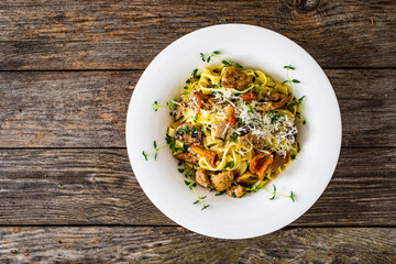 Tagliatelle with fried chicken breast nuggets, parmesan cheese and white mushrooms served on wooden table 