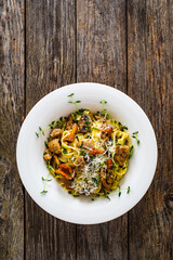 Tagliatelle with fried chicken breast nuggets, parmesan cheese and white mushrooms served on wooden table 