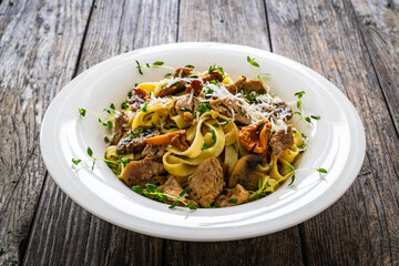 Tagliatelle with fried chicken breast nuggets, parmesan cheese and white mushrooms served on wooden table 