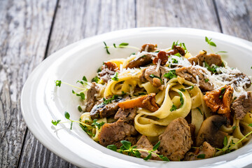 Tagliatelle with fried chicken breast nuggets, parmesan cheese and white mushrooms served on wooden table 
