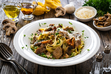 Tagliatelle with fried chicken breast nuggets, parmesan cheese and white mushrooms served on wooden table 