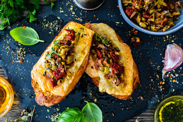 Tasty sandwiches - baked bread with cheese, olives, sun dried tomatoes and thyme on wooden table
