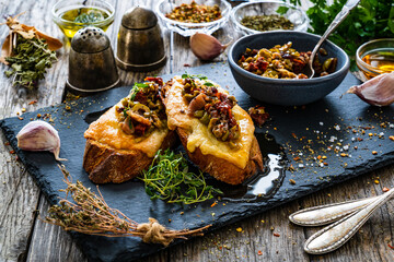 Tasty sandwiches - baked bread with cheese, olives, sun dried tomatoes and thyme on wooden table

