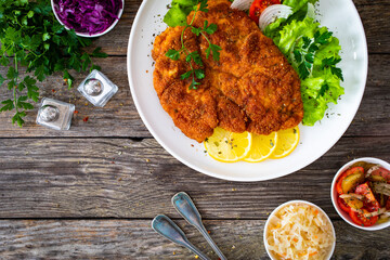 Breaded fried pork chop with cabbage salad and greens on wooden table
