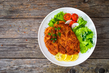 Breaded fried pork chop with cabbage salad and greens on wooden table
