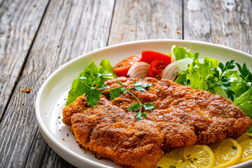 Breaded fried pork chop with cabbage salad and greens on wooden table
