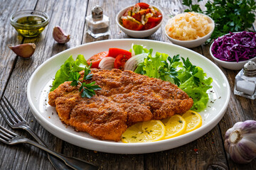 Breaded fried pork chop with cabbage salad and greens on wooden table
