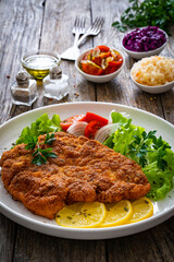 Breaded fried pork chop with cabbage salad and greens on wooden table
