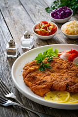 Breaded fried pork chop with cabbage salad and greens on wooden table

