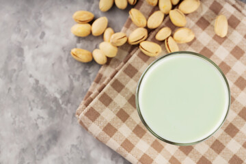 Fototapeta na wymiar Pistachio milk in a glass on a gray concrete background. Organic lactose free pistachio milk and pistachios. Top view. Copy space