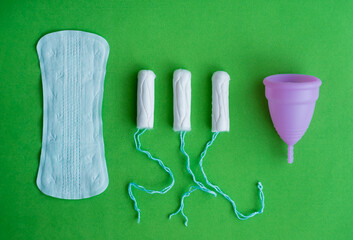 Pads, menstrual cup, tampons on a green background, concept of critical days