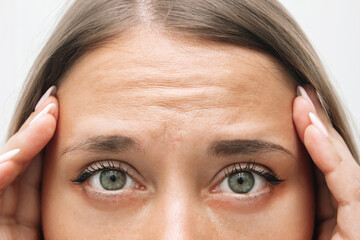 Young caucasian worried woman touching the forehead demonstrating wrinkles on her face on a white...