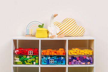 White shelving with colorful storage baskets and transparent boxes in children room. Rainbow toys in stylish baskets and plastic containers. Organizing and Storage Ideas in playroom. Interior design.