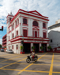 Colonial fire station building. In front of the building on the street a woman in a helmet on a motorcycle. sunny day. georgetown. Penang. Malaysia