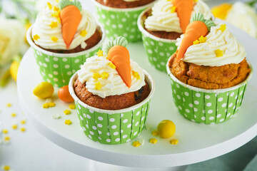 Carrot cake cupcakes for Easter. Carrot cupcakes with cream cheese frosting decorated with tiny marzipan carrots on white background. Happy Easter and spring holiday concept. Holydays homemade dessert