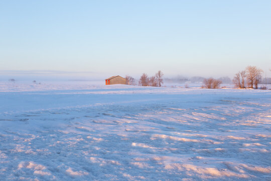 Pretty winter landscape with small wooden barn in snowy field seen at dawn, Beaumont, Bellechasse County, Quebec, Canada