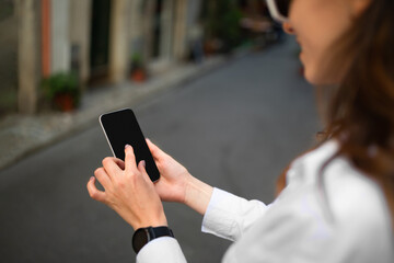 Smiling millennial european woman tourist in hat and sunglasses typing on smartphone with blank screen
