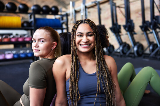 Smiling young women sitting back to back at the gym