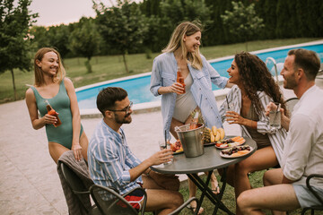 Group of young people cheering with cider by the pool in the garden