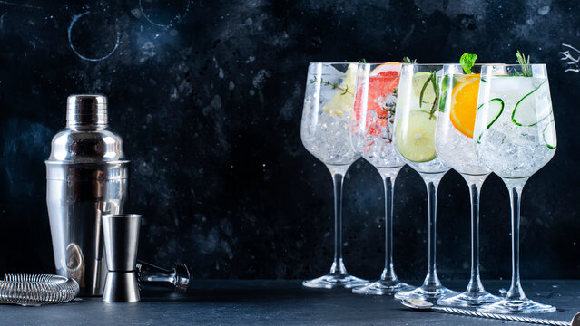 Gin tonic cocktails set. Trendy drinks with lime, lemon, grapefruit, orange, cucumber, soda and spicy herbs in wine glasses, black background