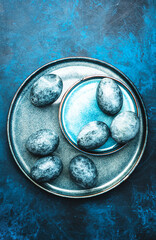 Easter composition with blue painted eggs on plate on blue background, top view