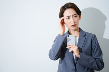 スマートフォンを持ちながら悩んでいる若い女性　ビジネスイメージ