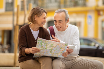 Happy Senior Couple Holding Travel Map Sitting Outdoors