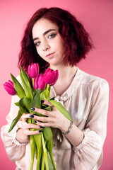 young beautiful girl holds a bouquet of flowers on a pink background.