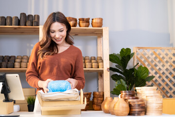 Young Asian female entrepreneur smile while talking on the phone and check customer order from online shopping inside of home office. New small business start up trend with online marketing.