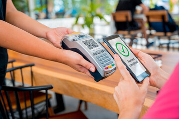Woman using contactless payment by mobile phone with QR code at cafe