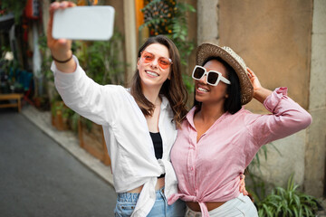 Smiling millennial african american and caucasian ladies tourists in hat and sunglasses taking selfie