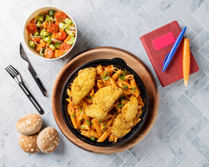 Chicken breast with penne pasta in a red sauce, served with salad and bread . Top View