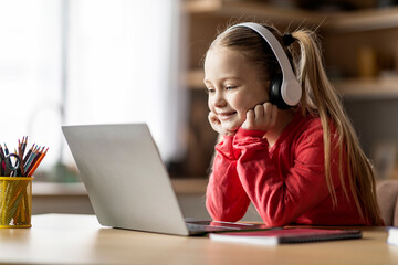 Cute Little Girl Wearing Wireless Headphones Study At Home With Laptop Computer - obrazy, fototapety, plakaty