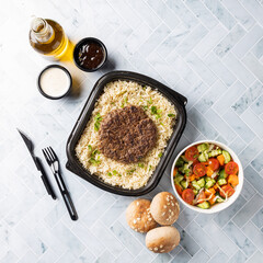 A healthy dish consisting of a plate of brown rice, topped with a grilled burger patty and served with a side of fresh salad, bread and flour.Perfect for social media or advertising campaigns.Top View