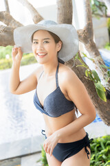 Happy smiling relaxed summer woman wearing bikini swimsuit with hat at swimming pool