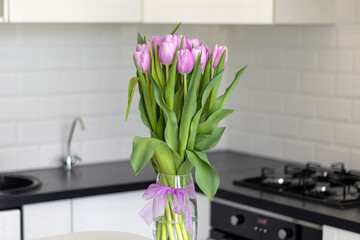 Bouquet of purple tulips in a clear vase against the background of a modern white kitchen