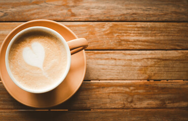 heart-shaped coffee latte In a brown cup with a saucer, placed on an old wooden table. That is ready to give you freshness every morning.