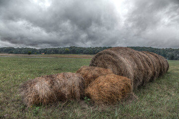 Hay Bale with Split Ends.  A row of hay bales is split on the end in two directions.  Falling apart into a loose scattering of of hay.  A marble sky with gobs of clouds of multi shades of gray and whi