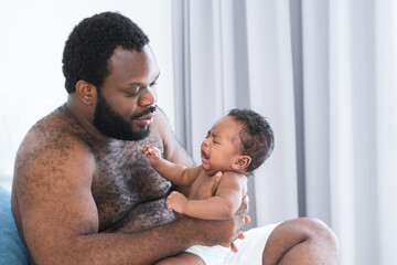 African middle aged bearded father is soothing newborn baby crying in his arms in bedroom at home....